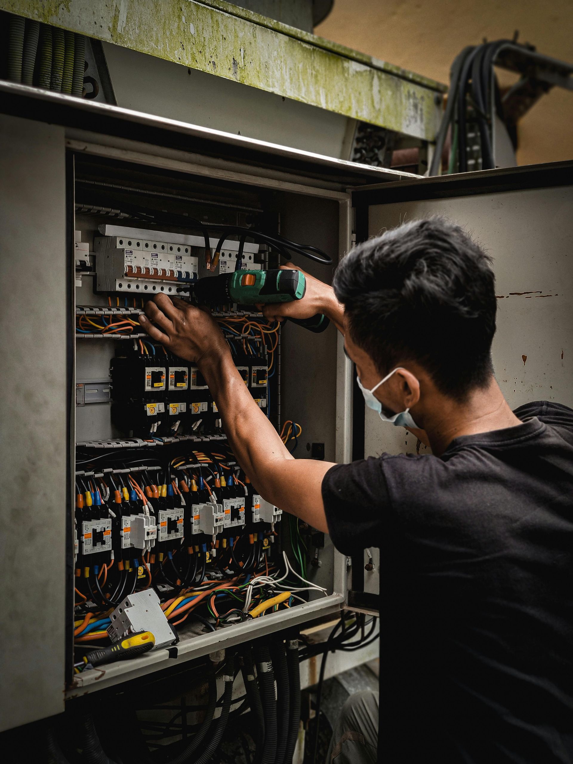 Technician inspecting an electrical control panel with exposed wiring and circuit breakers outdoors