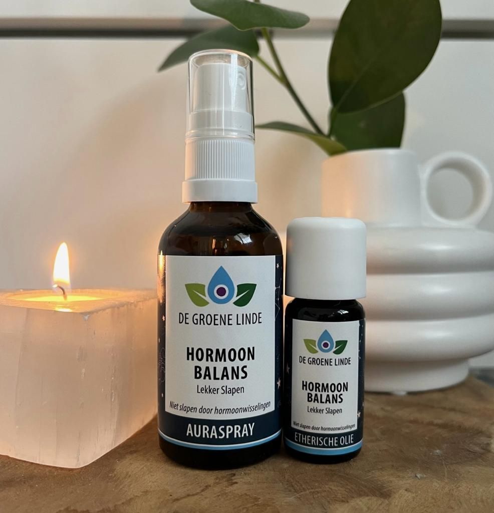 Twee flesjes met kruidengeneesmiddelen staan ​​op een tafel naast een brandende kaars en een witte vaas met plantenbladeren.