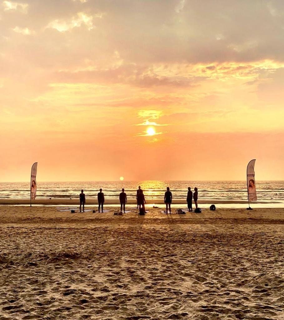 Zonsondergang boven een strand met silhouetten van mensen die langs de kustlijn wandelen en een warme gouden hemel.