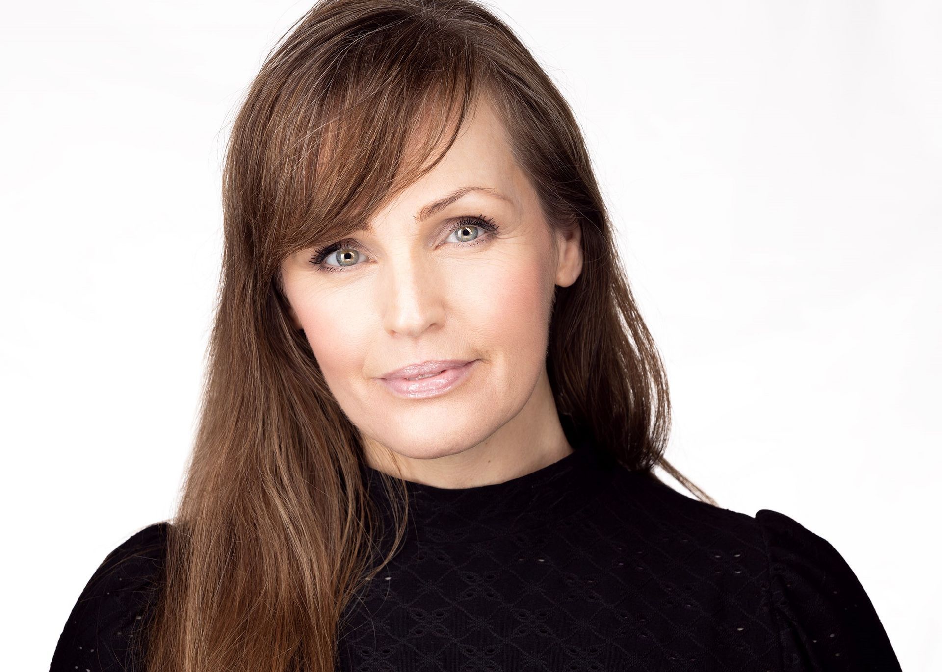 Portret van een vrouw met lang bruin haar in een zwarte top tegen een witte achtergrond.