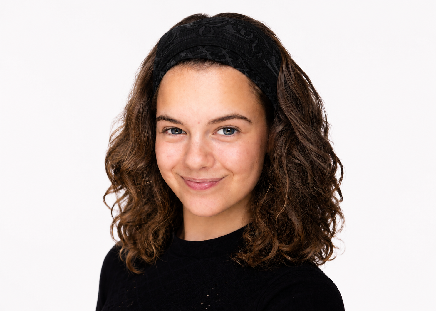 Lachende vrouw met krullend donker haar, gekleed in een zwarte top, tegen een witte achtergrond.