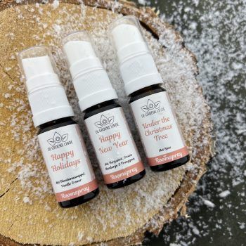 Drie parfumverstuivers met feestelijke geuren op een houten schijf met sneeuwvlokversieringen.