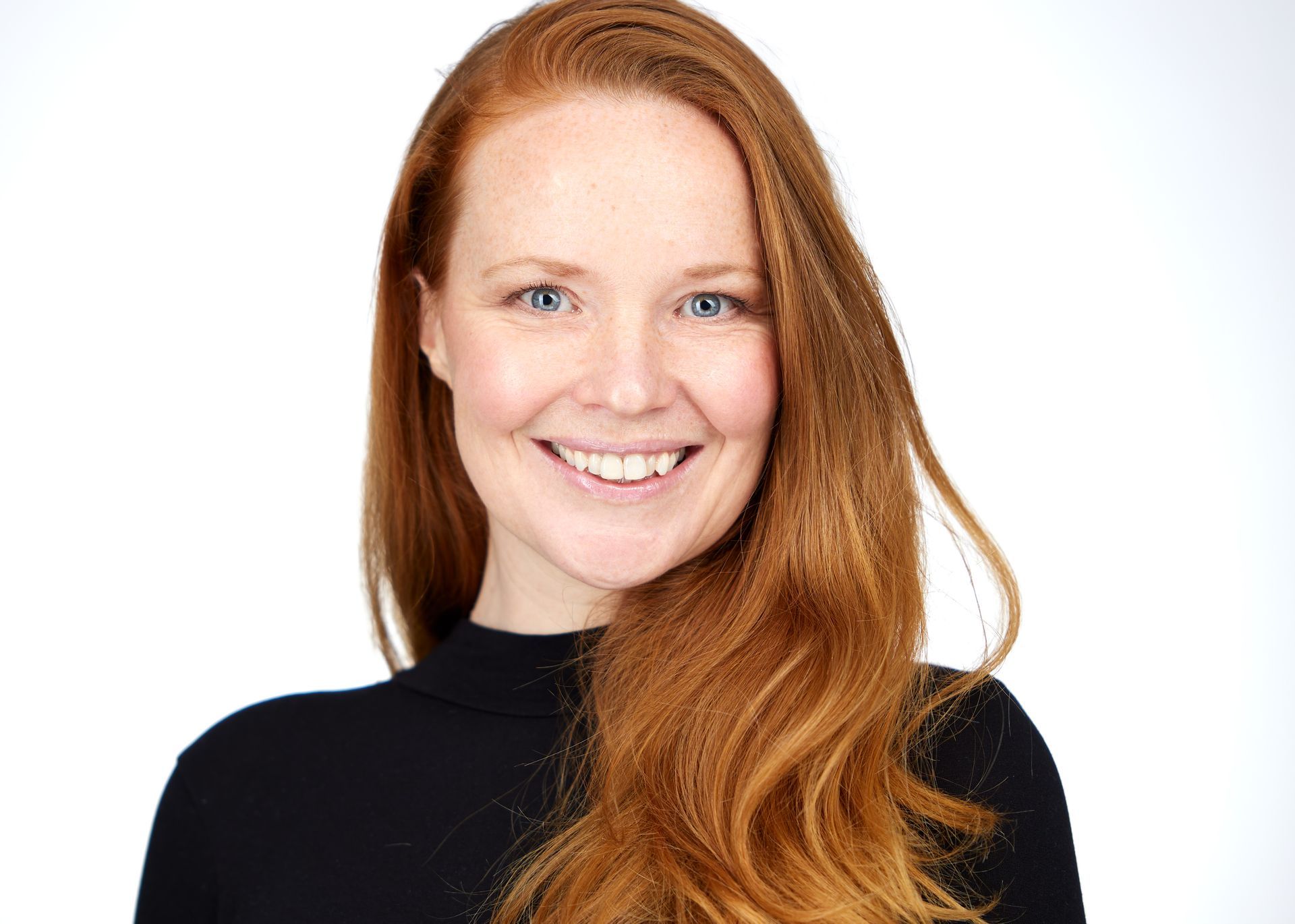 Lachende vrouw met lang rood haar, gekleed in een zwarte top, tegen een witte achtergrond.