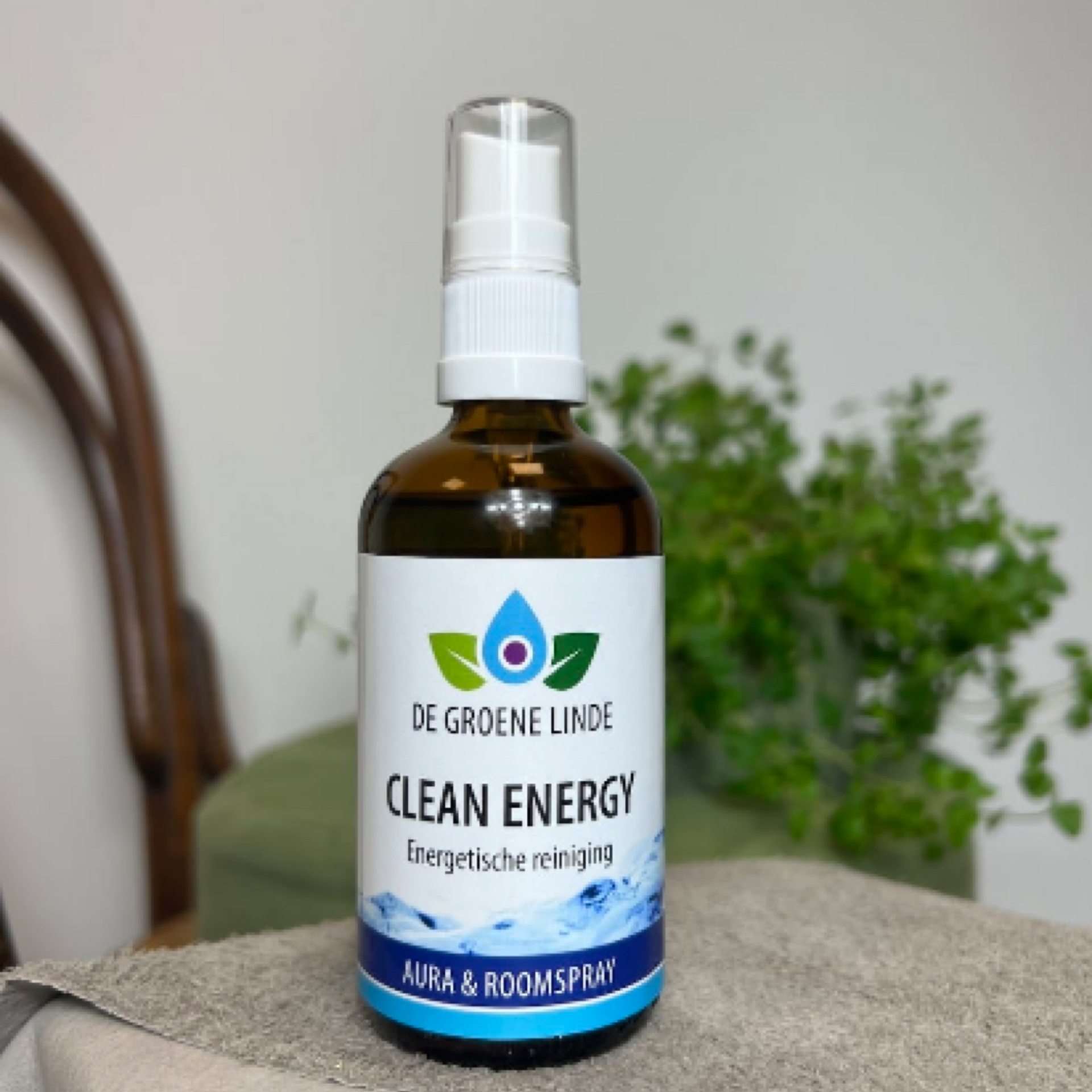 Een amberkleurige spuitfles De Groene Linde Clean Energy aura- en kamerspray op een tafel, met planten erachter.