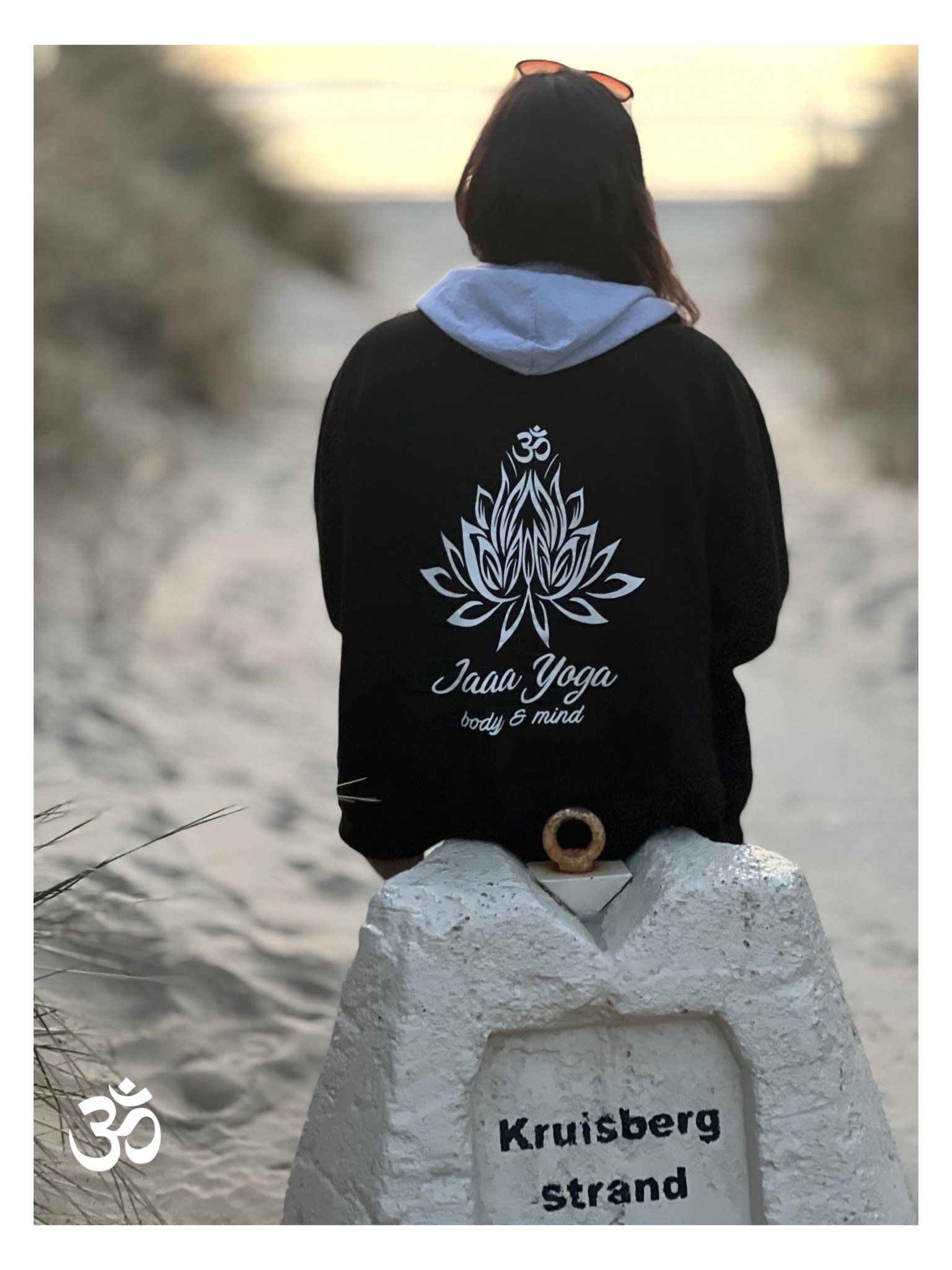 Een persoon in een zwarte hoodie zit op een stenen markering en kijkt uit over een besneeuwd pad bij zonsondergang.