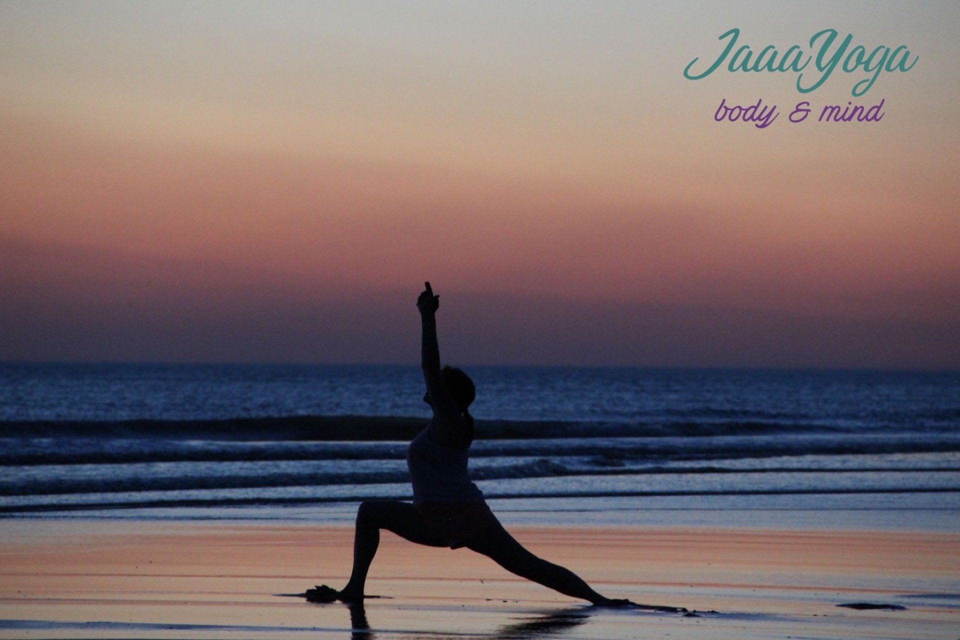 Silhouet van een persoon die een yoga-uitvalshouding aanneemt op een strand bij zonsondergang, met een pastelkleurige lucht en oceaangolven.