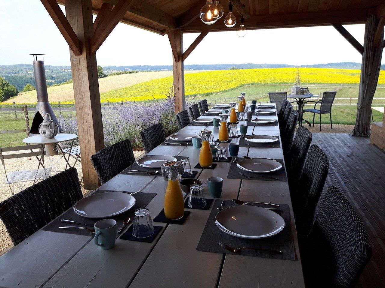Eettafel buiten onder een overdekt terras met uitzicht op een heldergroen veld en heuvels in de verte.