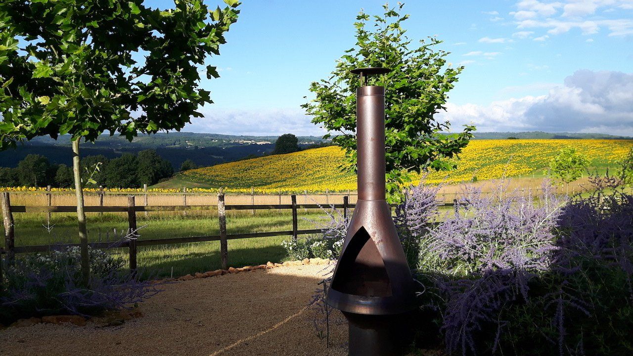 Terras met uitzicht op groene heuvels en wilde bloemen, met een hoge metalen terrashaard op de voorgrond.