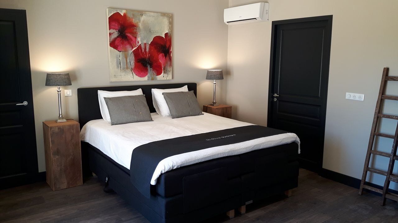 Moderne slaapkamer met een bed, donkere meubels, wandlampen en een rood bloemenkunstwerk boven het hoofdeinde.