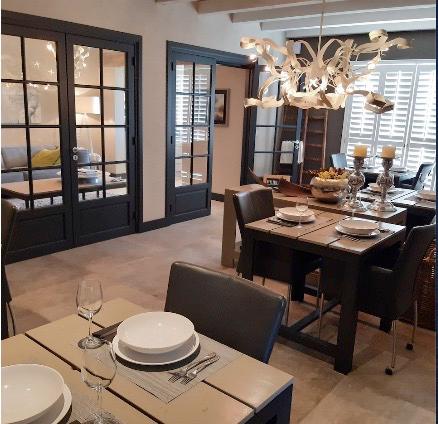 Elegante eetkamer met donkerhouten tafel, gedekt servies en glazen deuren die toegang geven tot een slaapkamer.