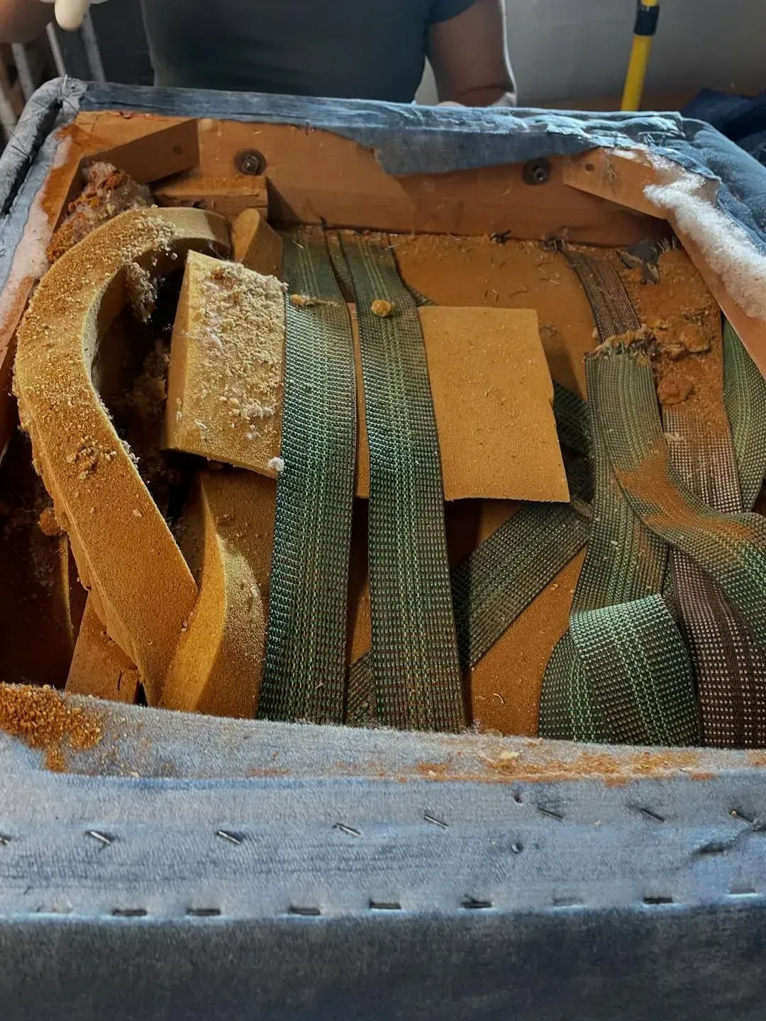 Box filled with tan and green woven material or straps, with a person partly visible behind it