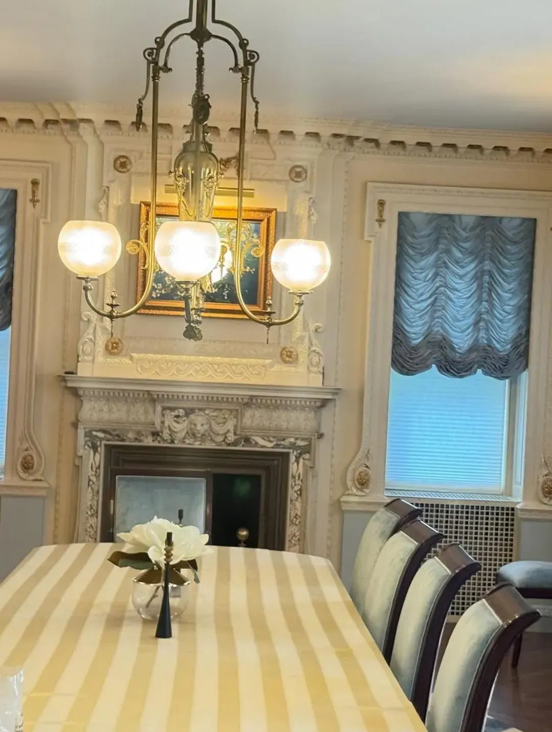 Elegant dining room with striped tablecloth, ornate chandelier, and marble fireplace on the far wall