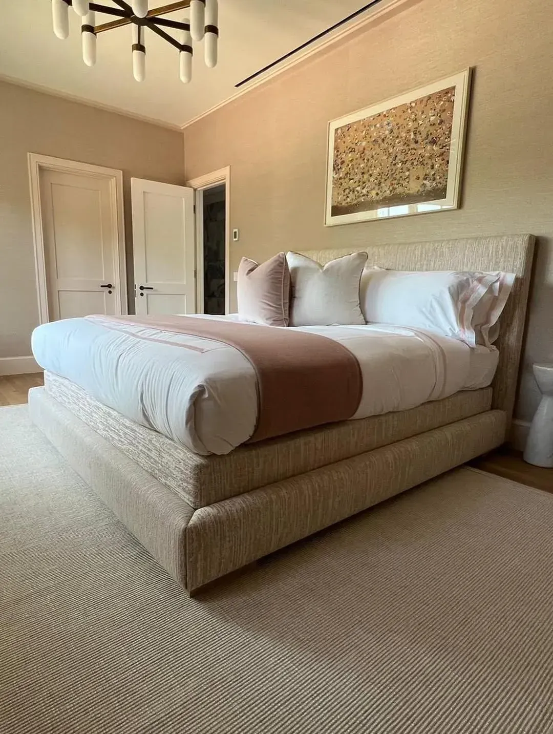 Elegant beige bedroom with a tufted bed, white bedding, brown throw, and framed wall art