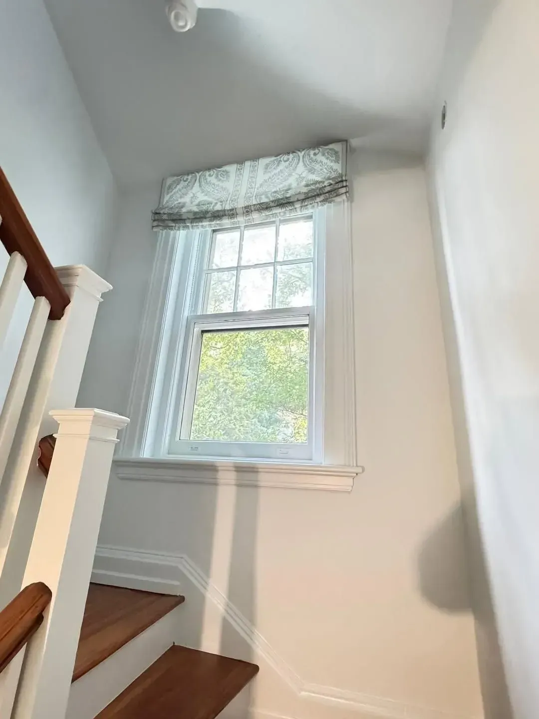 Stairway landing with a window, white walls, and wooden banister in a bright home interior