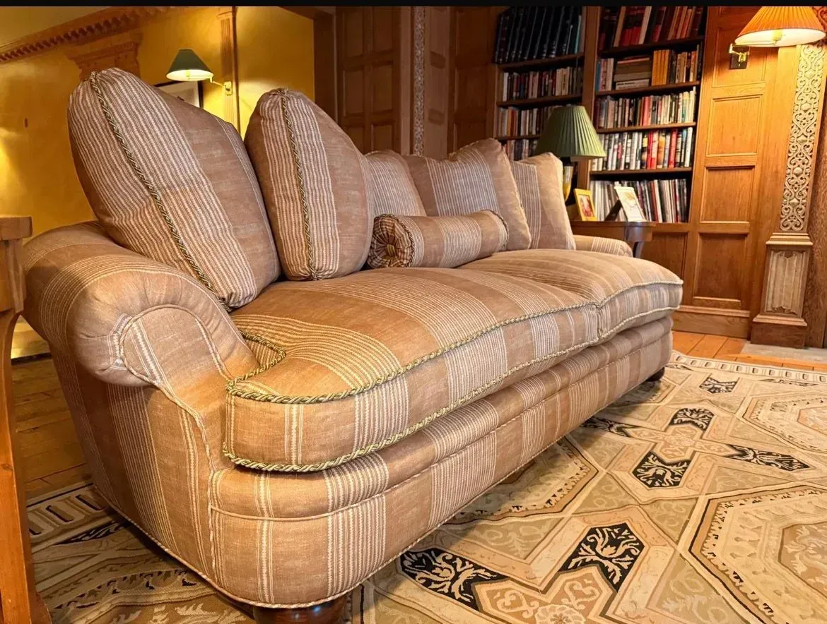 Patterned tan sofa in a cozy wood-paneled room with bookshelves and a rug.