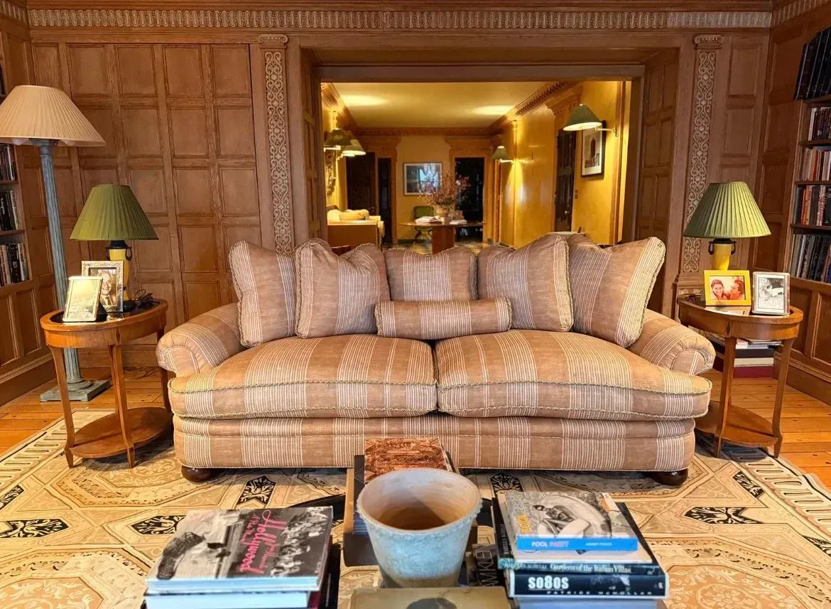 Elegant living room with plaid sofa, wood-paneled walls, and warm lamps across a central hallway