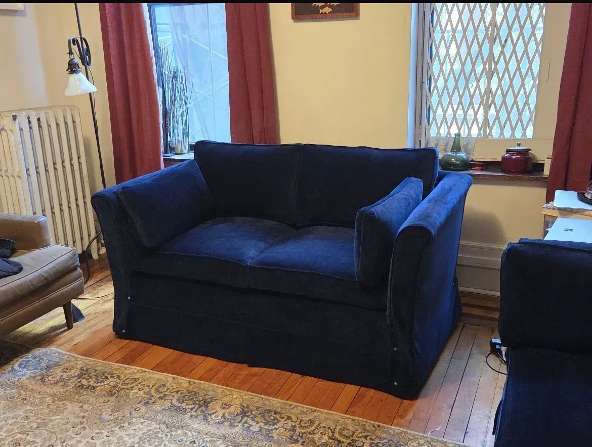 Blue loveseat in a cozy living room with patterned rug, windows, and warm curtains.