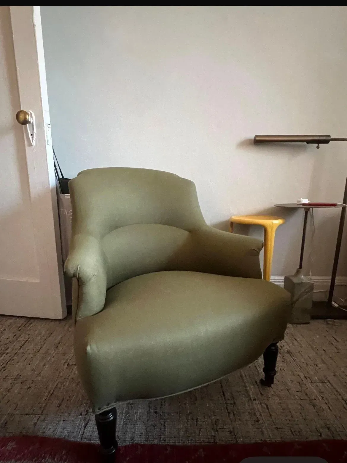 Green upholstered chair in a room beside an open door and a small side table