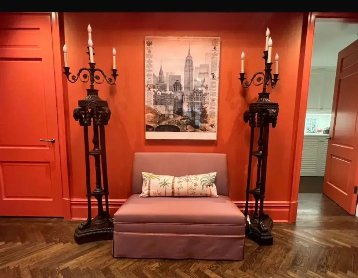 Red room with pink chair, framed city art, and ornate black floor lamps on either side.