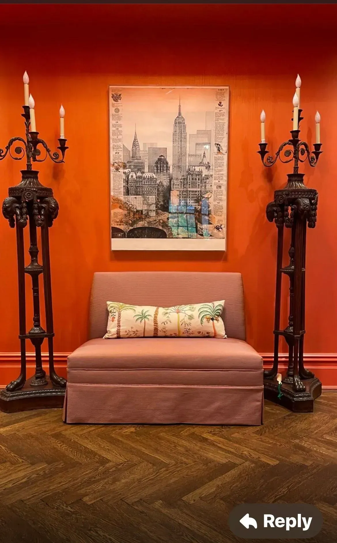 Elegant orange room with twin black candle stands, a small bench, and a cityscape painting on the wall