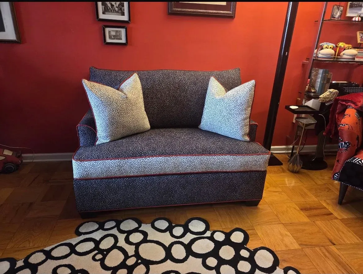 Patterned loveseat against a red wall, with a black-and-white rug in the foreground and hardwood floor.