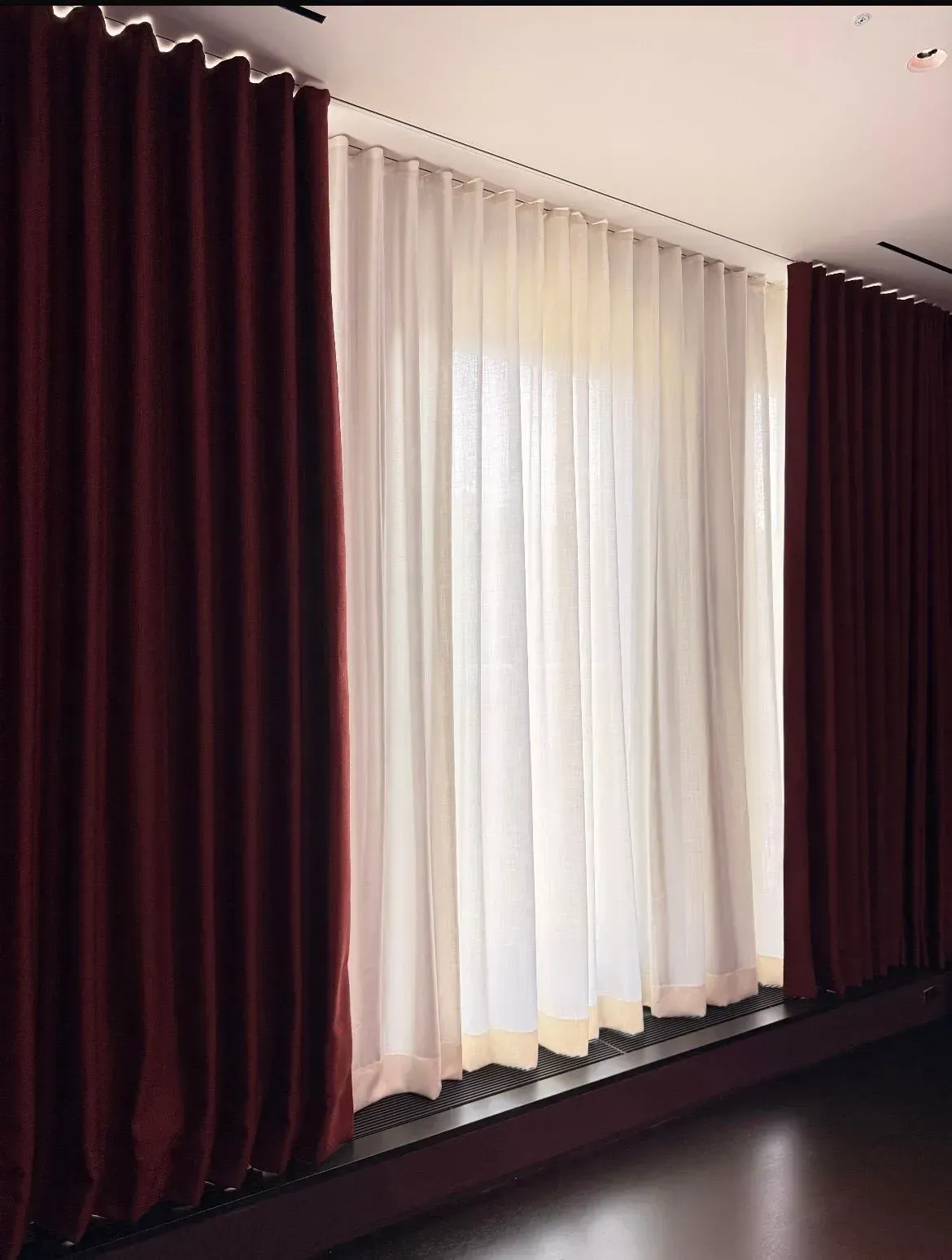 Floor-to-ceiling burgundy and white curtains covering a large window in a room