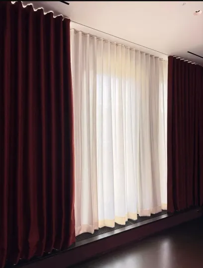 White sheer curtains framed by dark burgundy drapes along a tall window in a dim room