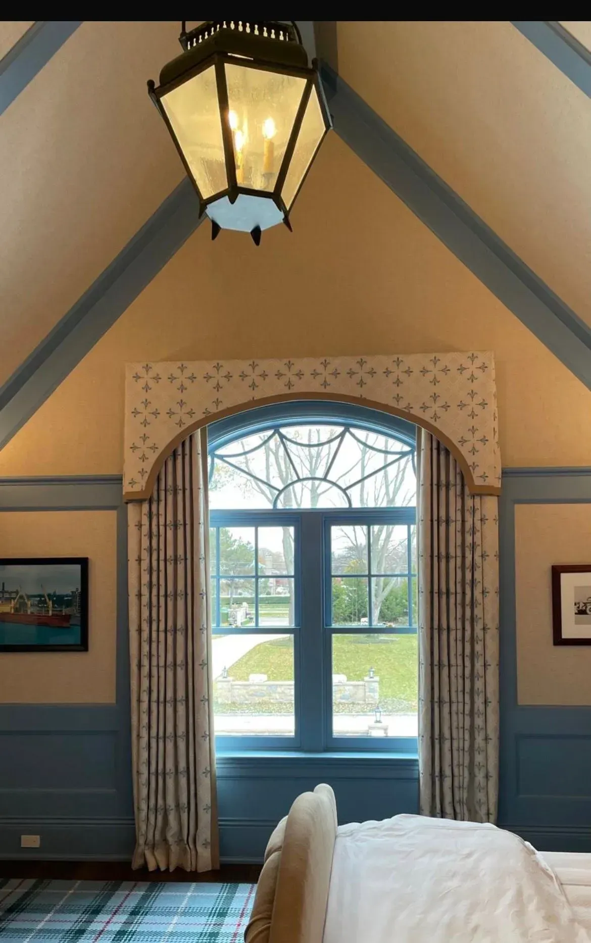 Cozy bedroom with a vaulted ceiling, hanging lantern, and a window framed by curtains and a blue sill