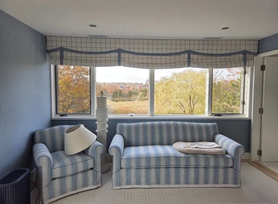 Blue-striped sofa and armchair in a bright room with large windows and autumn trees outside