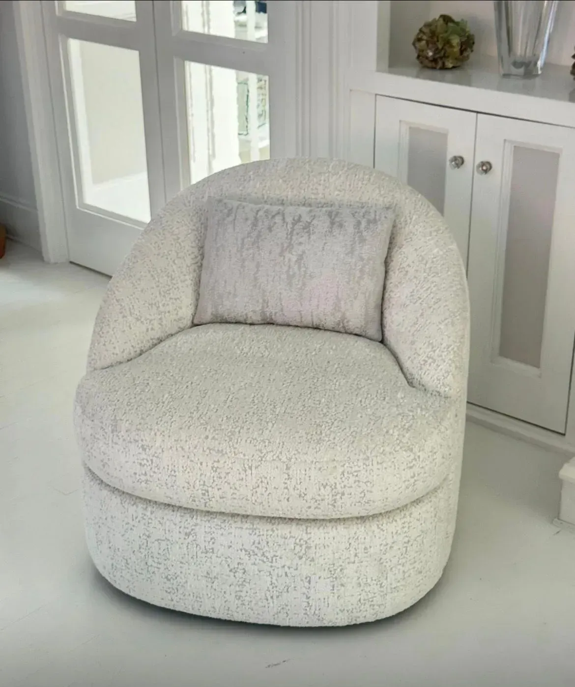 White upholstered swivel chair with a gray pillow in a bright room