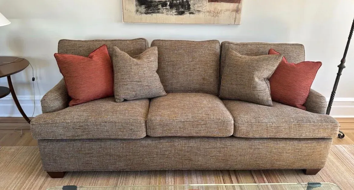 Beige patterned sofa with rust and taupe throw pillows in a bright living room