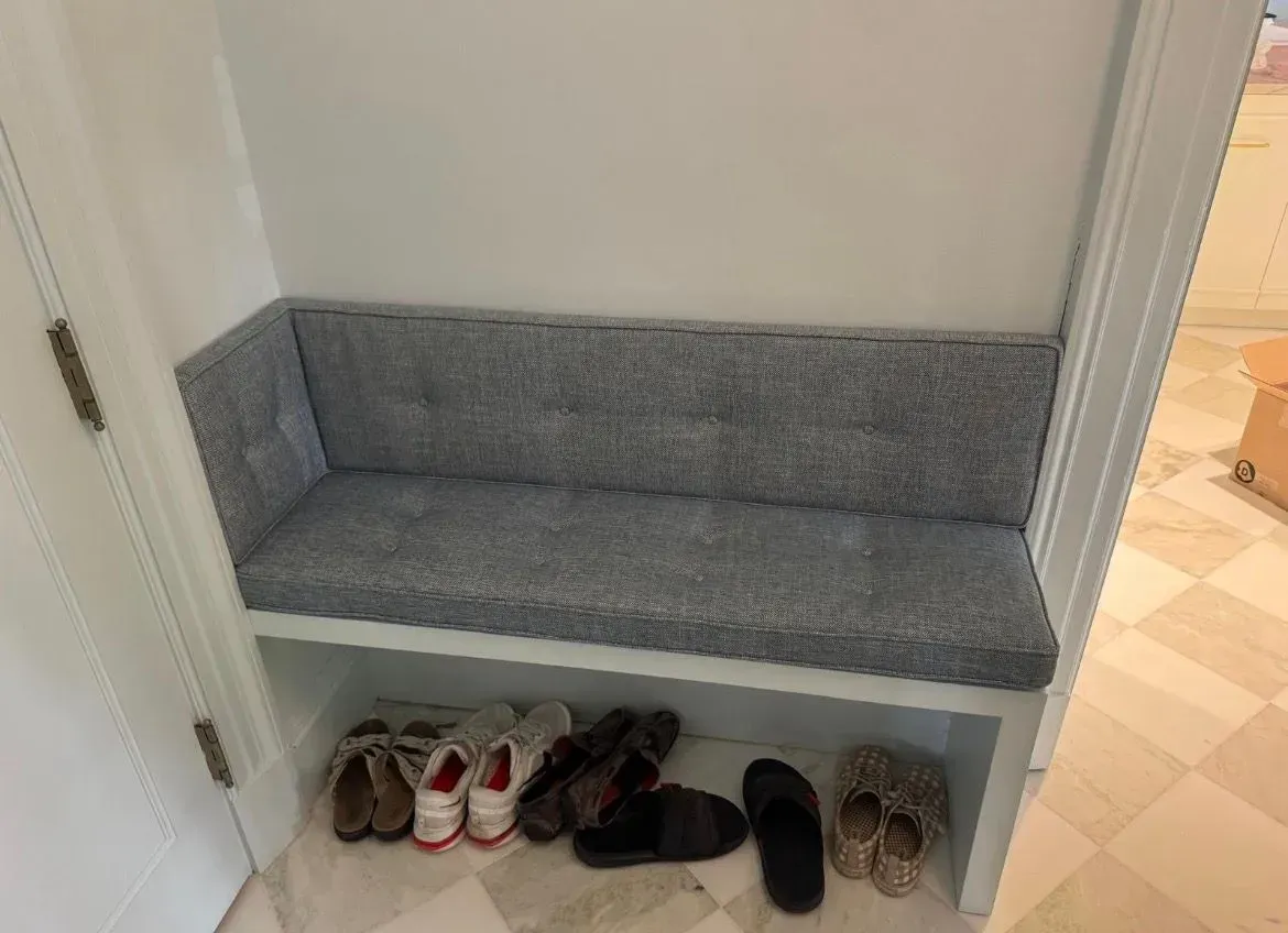 Gray cushioned bench with cubby shelf of shoes in a hallway nook