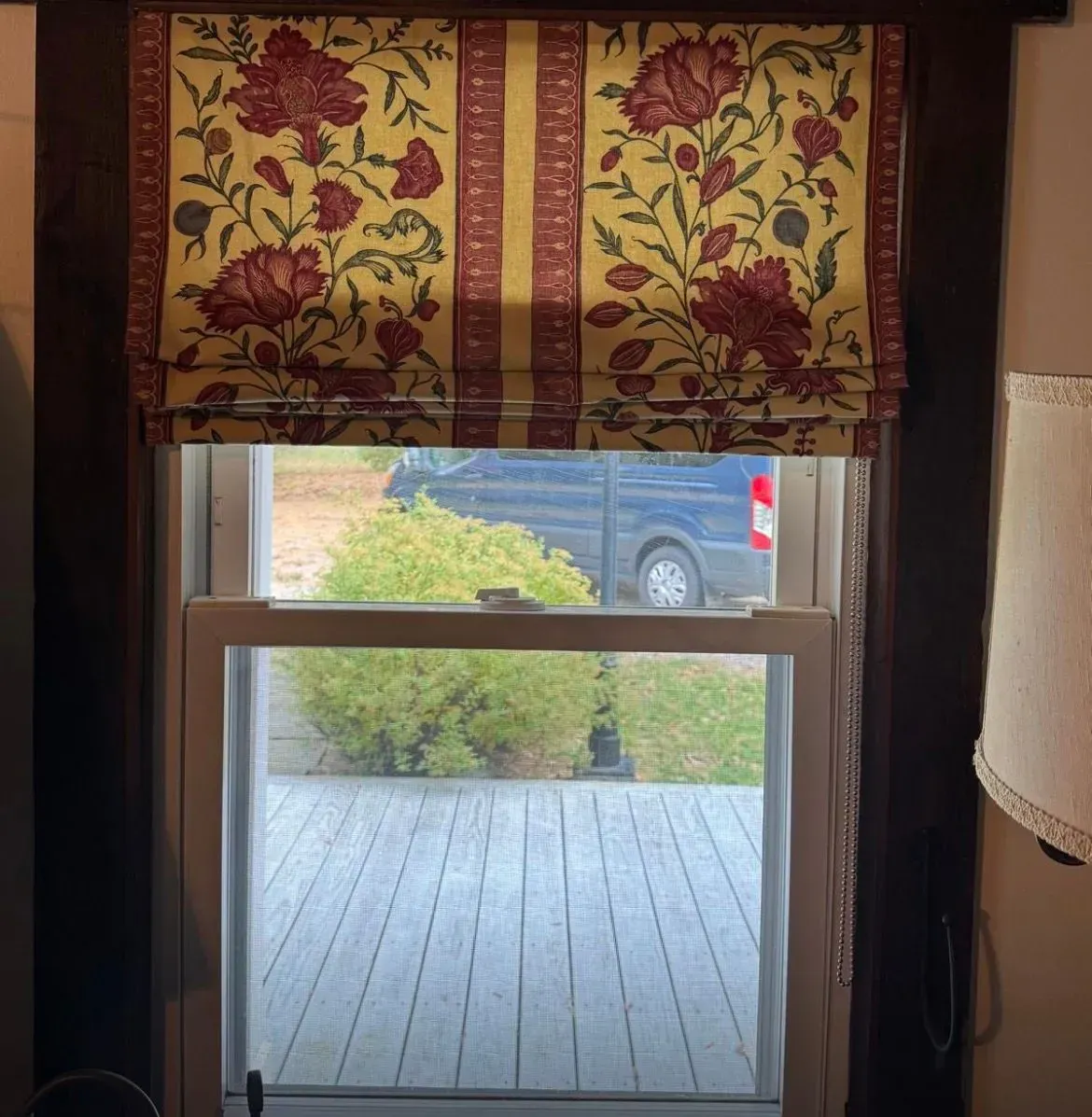 Floral window valance above a glass door, looking out to a wooden deck and parked car beyond.