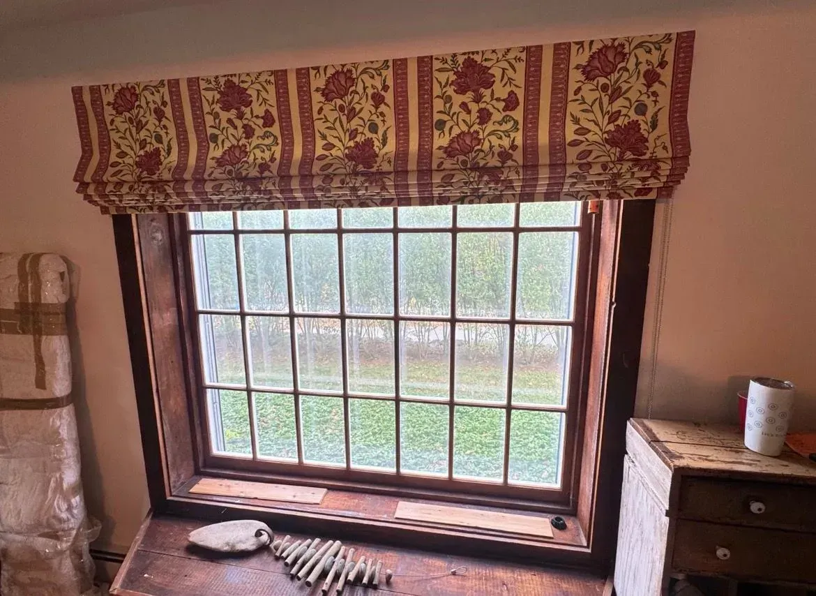 Rustic room with a barred window, patterned valance, wooden dresser, and striped cat on the sill