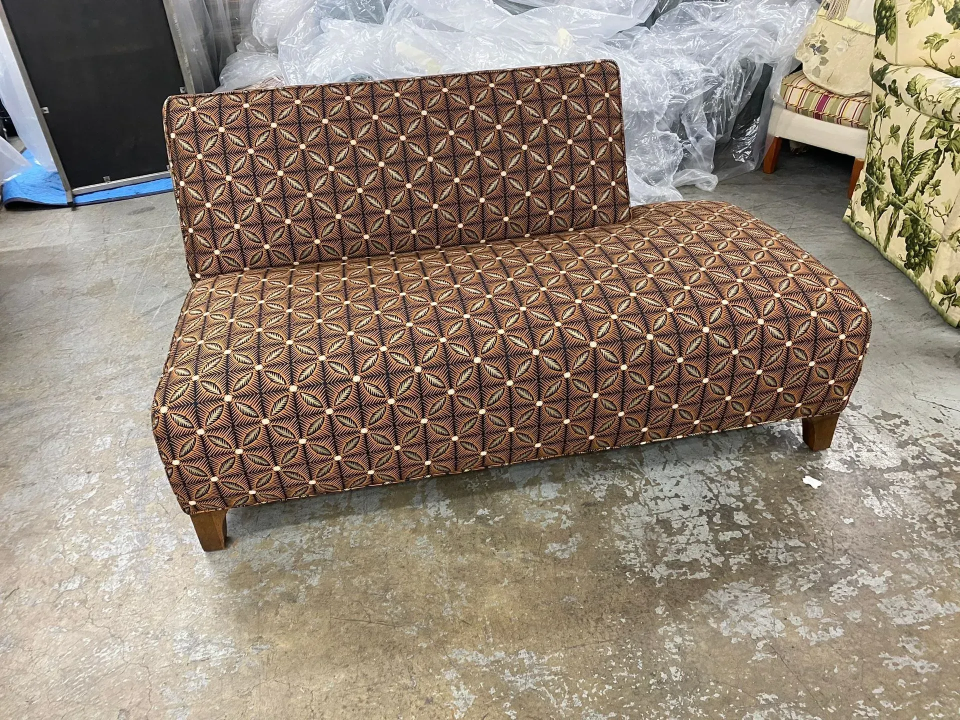 Brown patterned sofa with a low back on a concrete floor in a workshop or storage area