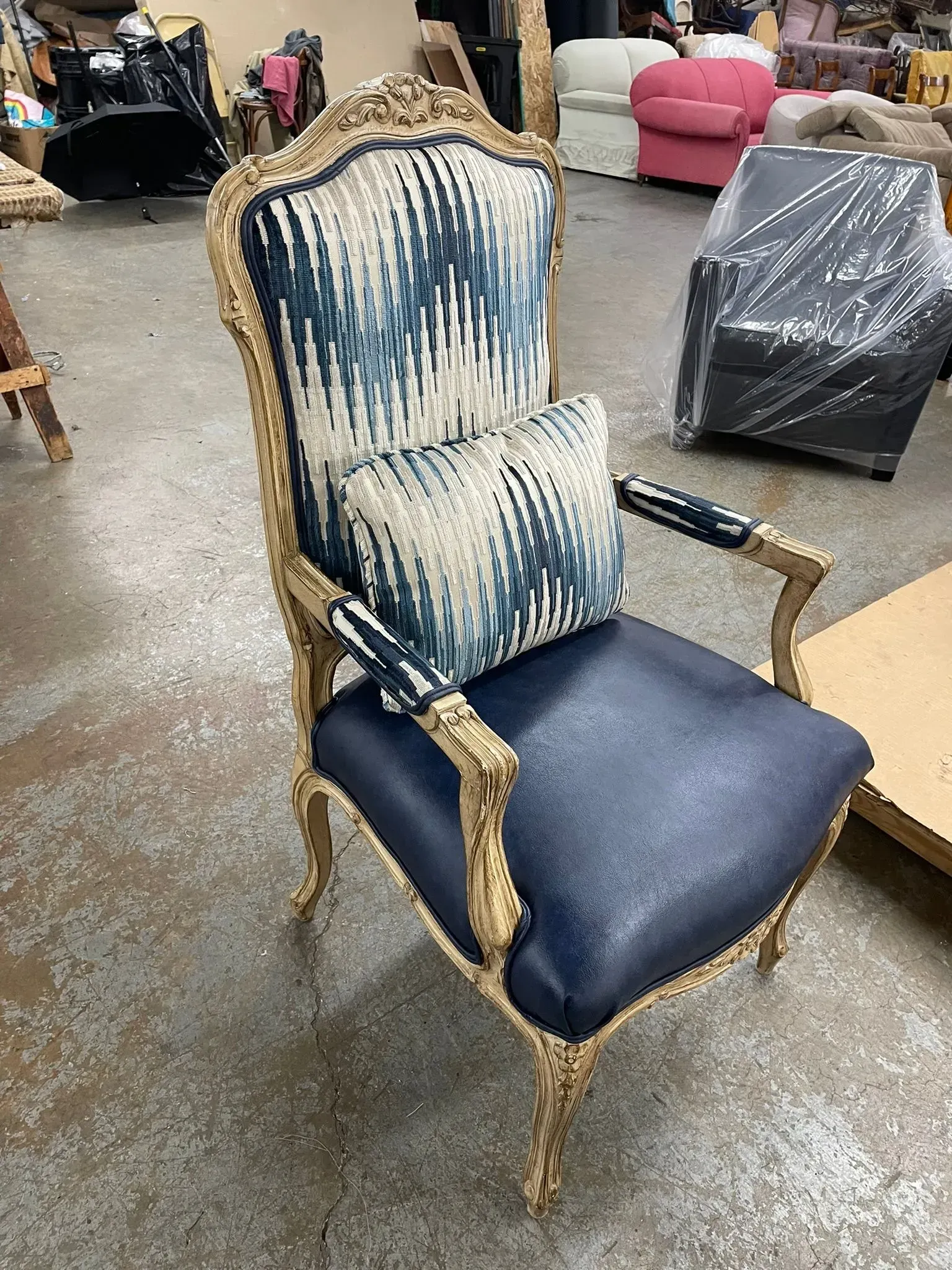Vintage upholstered armchair with blue patterned back and dark seat, standing in a warehouse-like room.