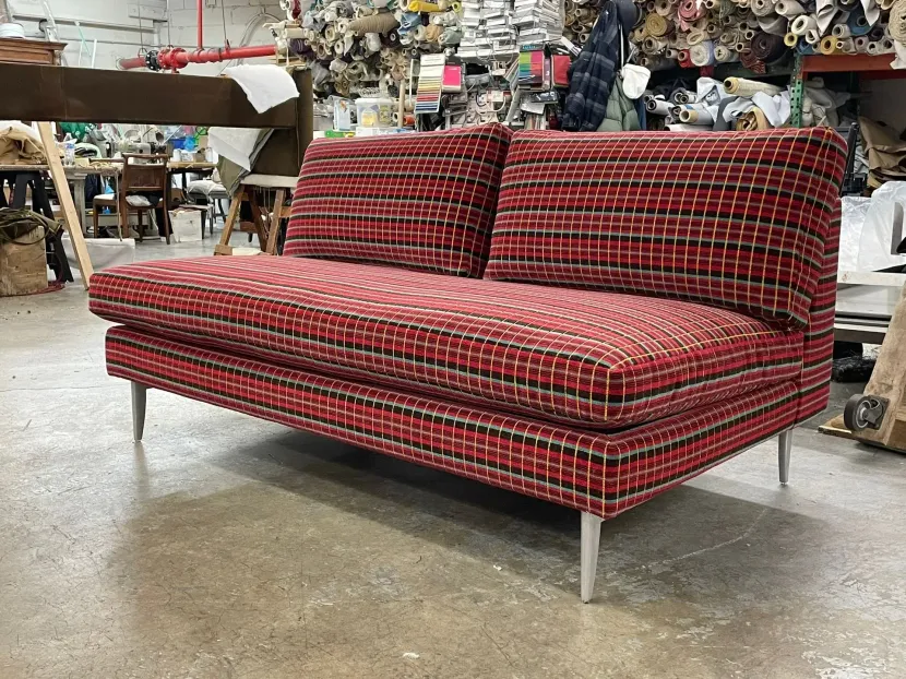 Red plaid upholstered sofa with metal legs in a warehouse showroom