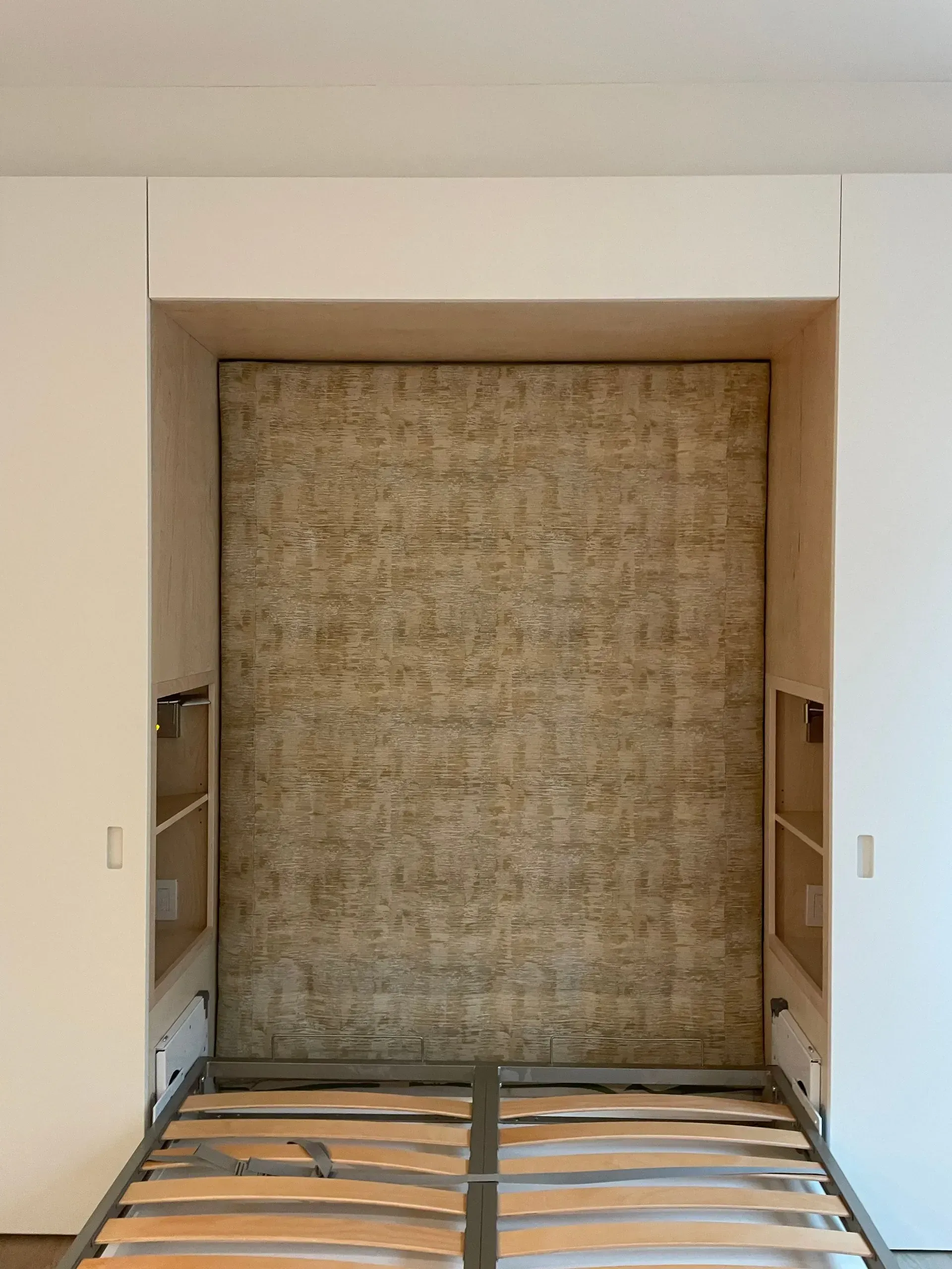 Built-in wall bed with woven headboard and wooden base in a recessed white alcove.