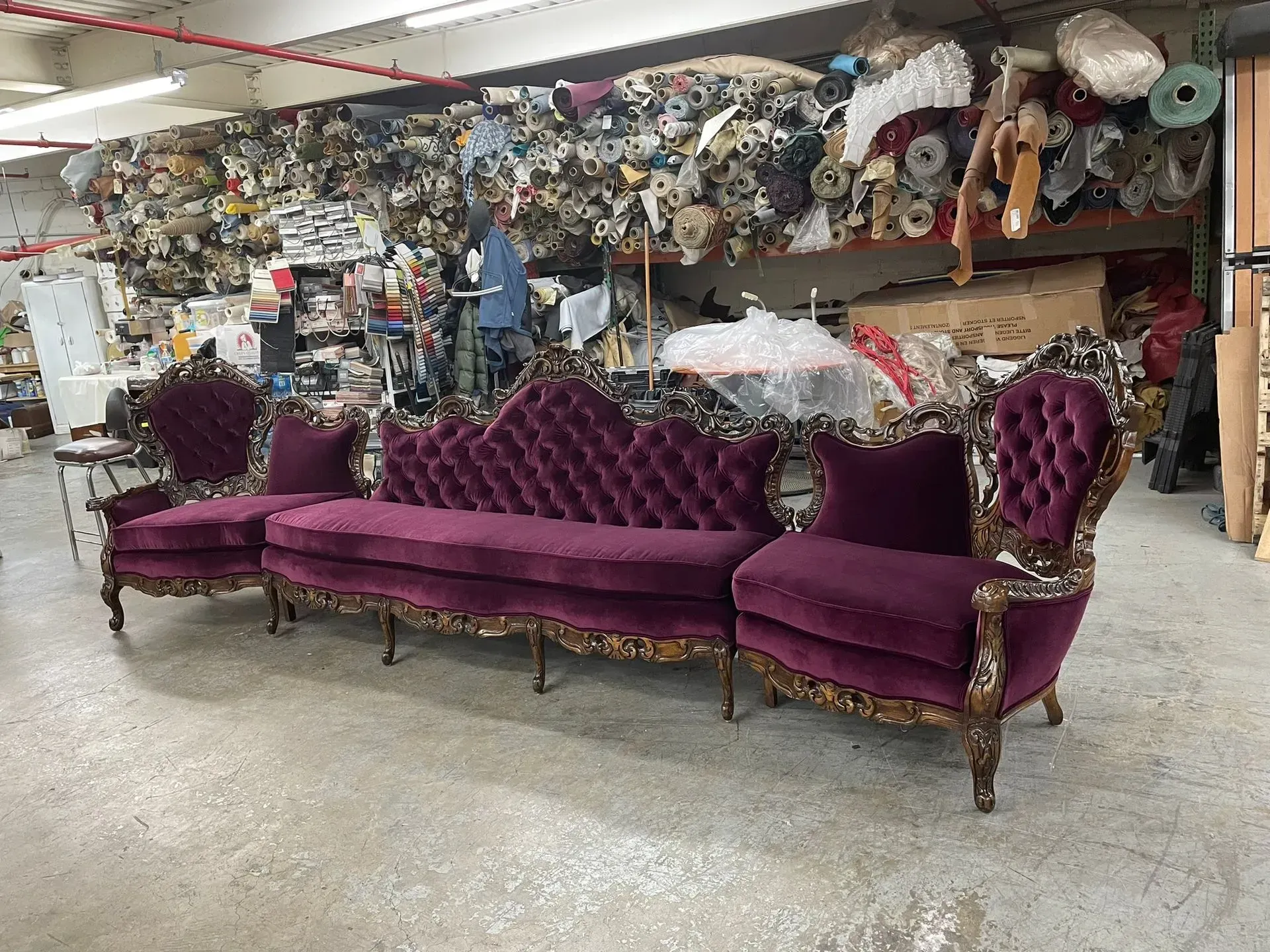 Purple Victorian-style sofa set in a cluttered warehouse or upholstery workshop