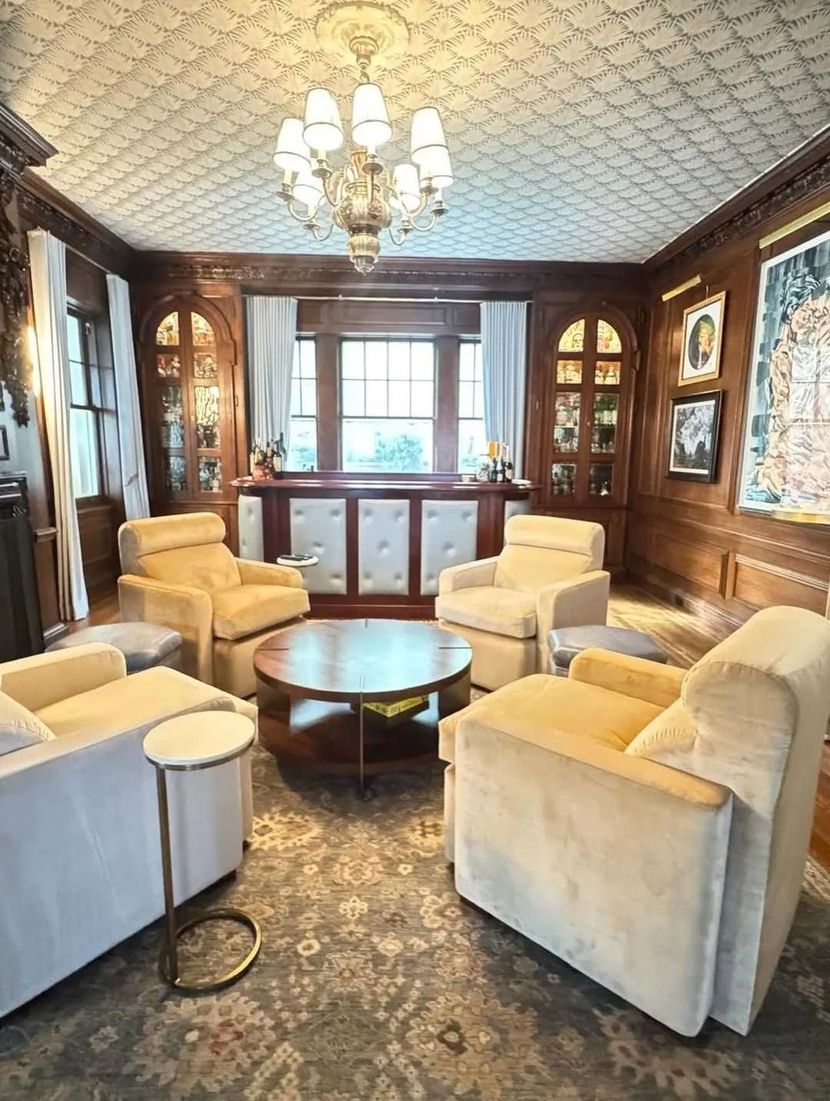 Elegant sitting room with cream chairs, round table, wood paneling, and chandelier by a window