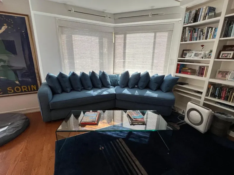 Bright living room with a blue sectional sofa, glass coffee table, bay windows, and built-in bookshelves.