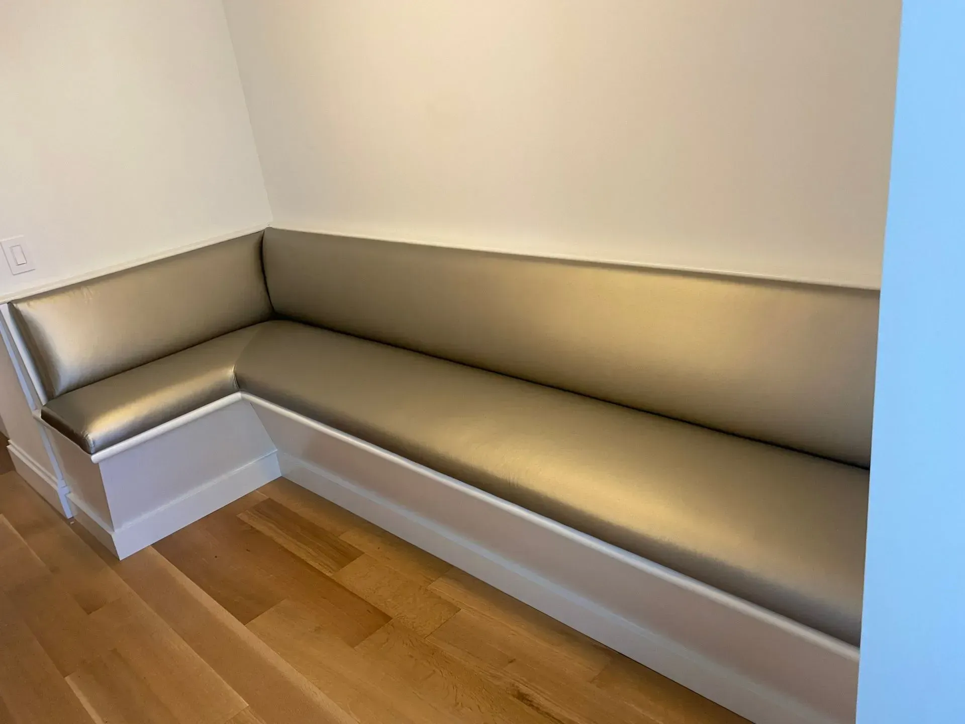 Built-in beige corner bench with cushioned seat in a wood-floored room