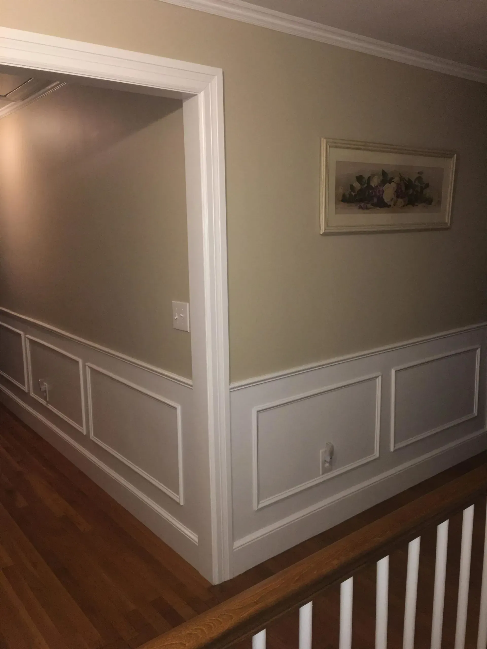 Empty beige hallway with white wainscoting, wood floors, and a framed picture on the wall