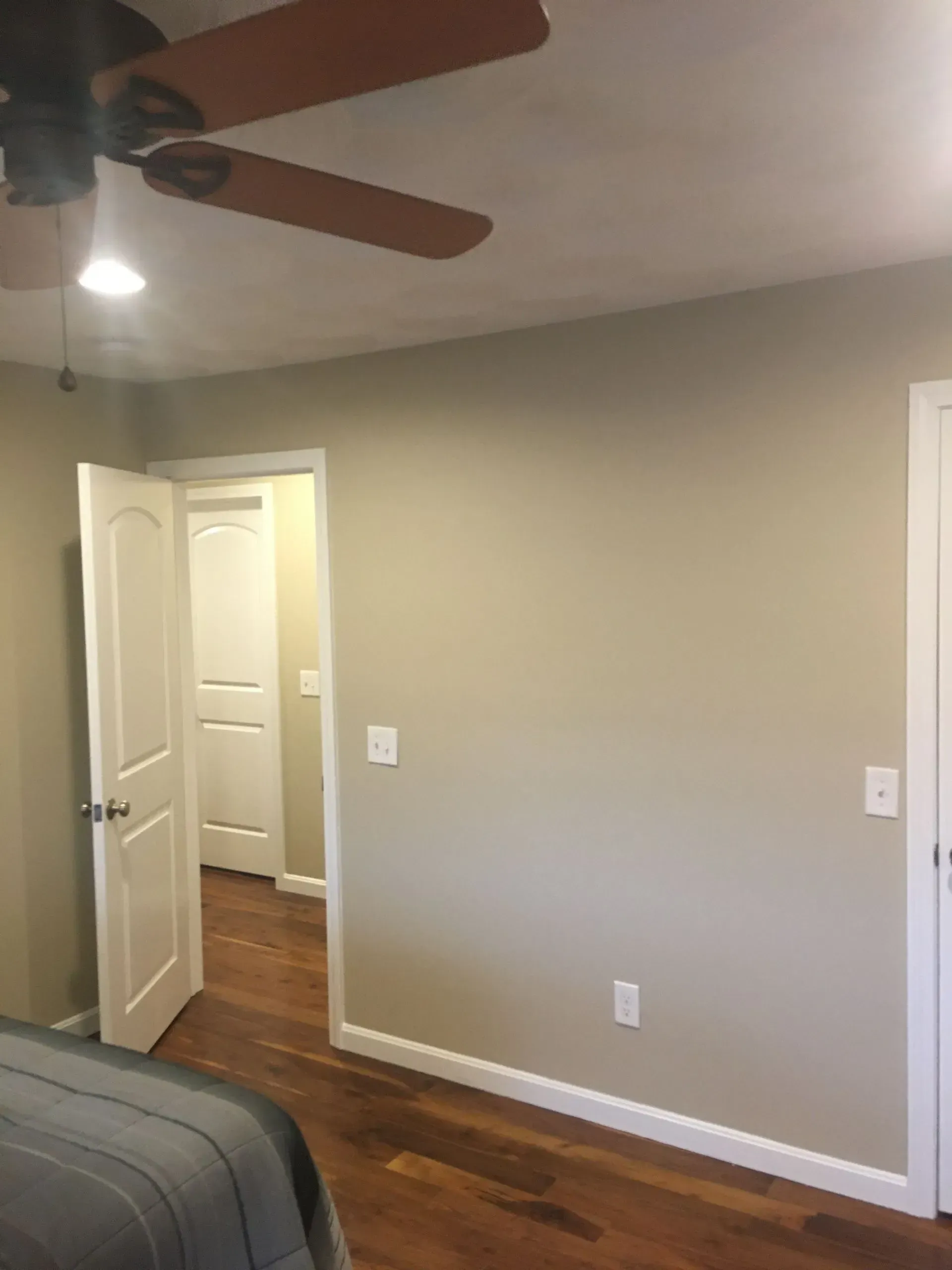 Empty beige bedroom with hardwood floors, white trim, open closet door, and ceiling fan.