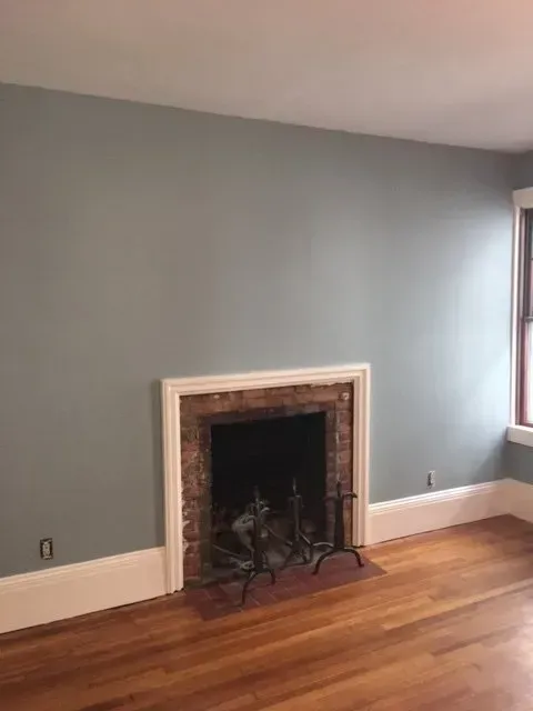 Empty room with blue-gray walls, hardwood floor, and a white-trimmed fireplace.
