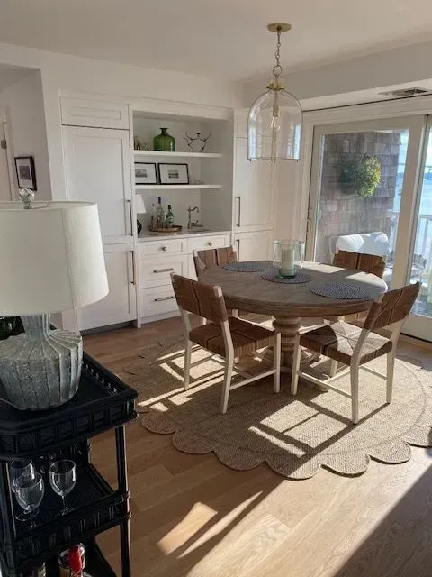 Bright dining room with wooden table, chairs, white built-ins, and sunlight through glass doors.