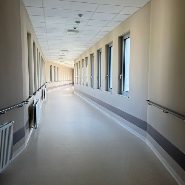Empty indoor corridor with windows, radiators, and beige walls