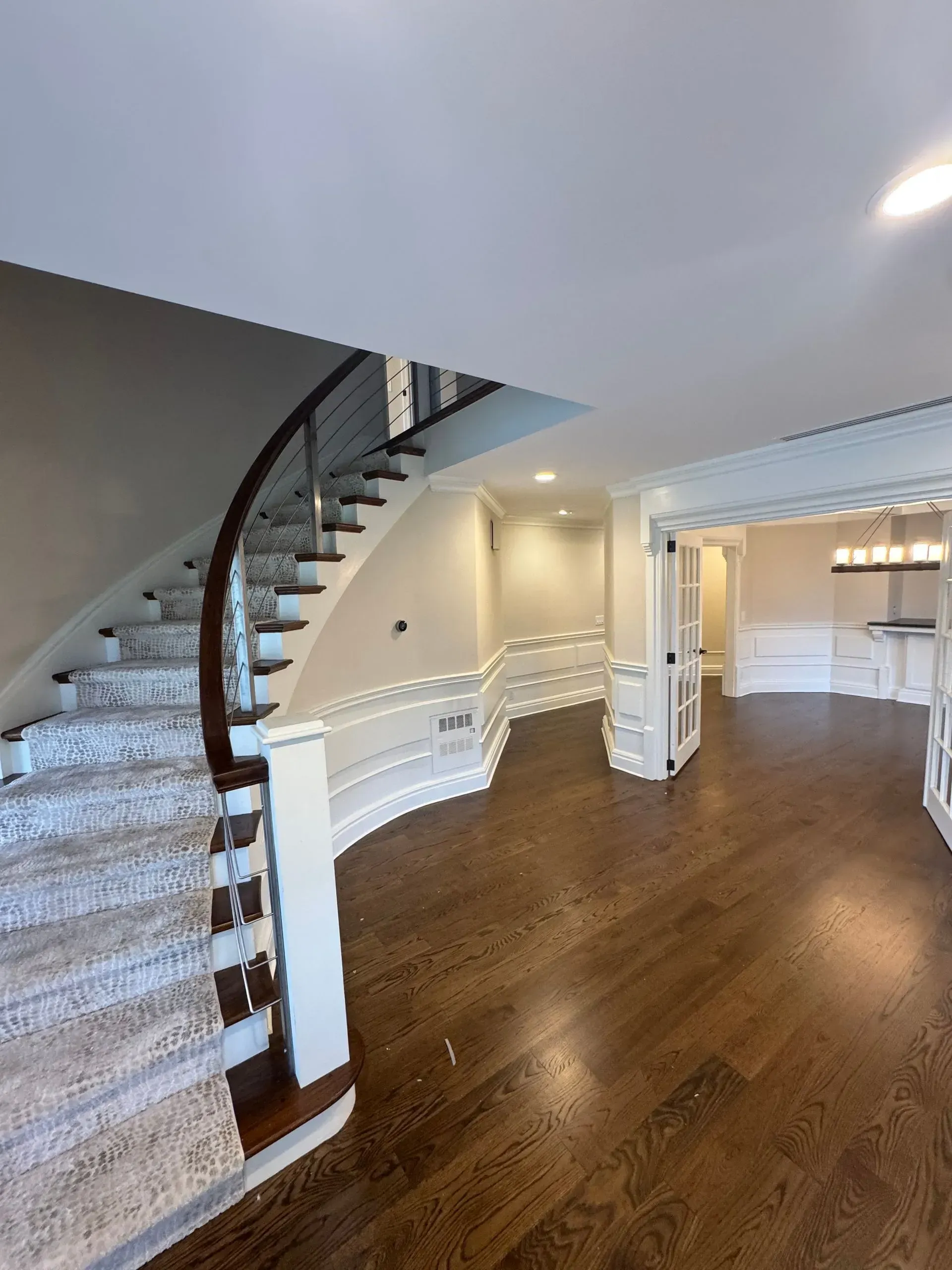 Spacious foyer with curved staircase, white trim, and dark hardwood floors leading to open rooms.