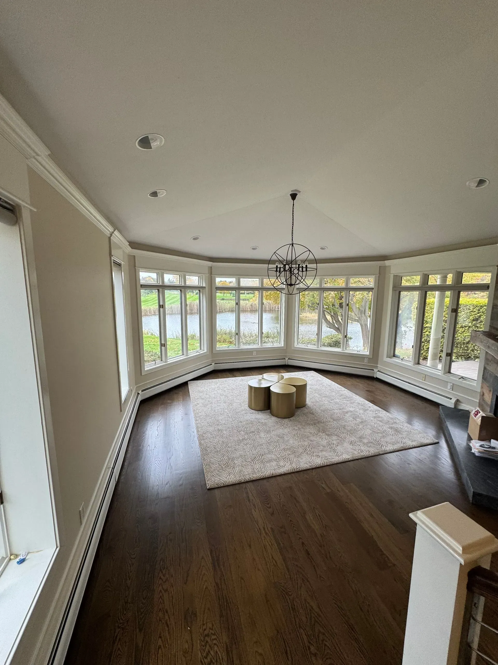 Bright sunroom with bay windows, dark wood floors, white rug, and chandelier.