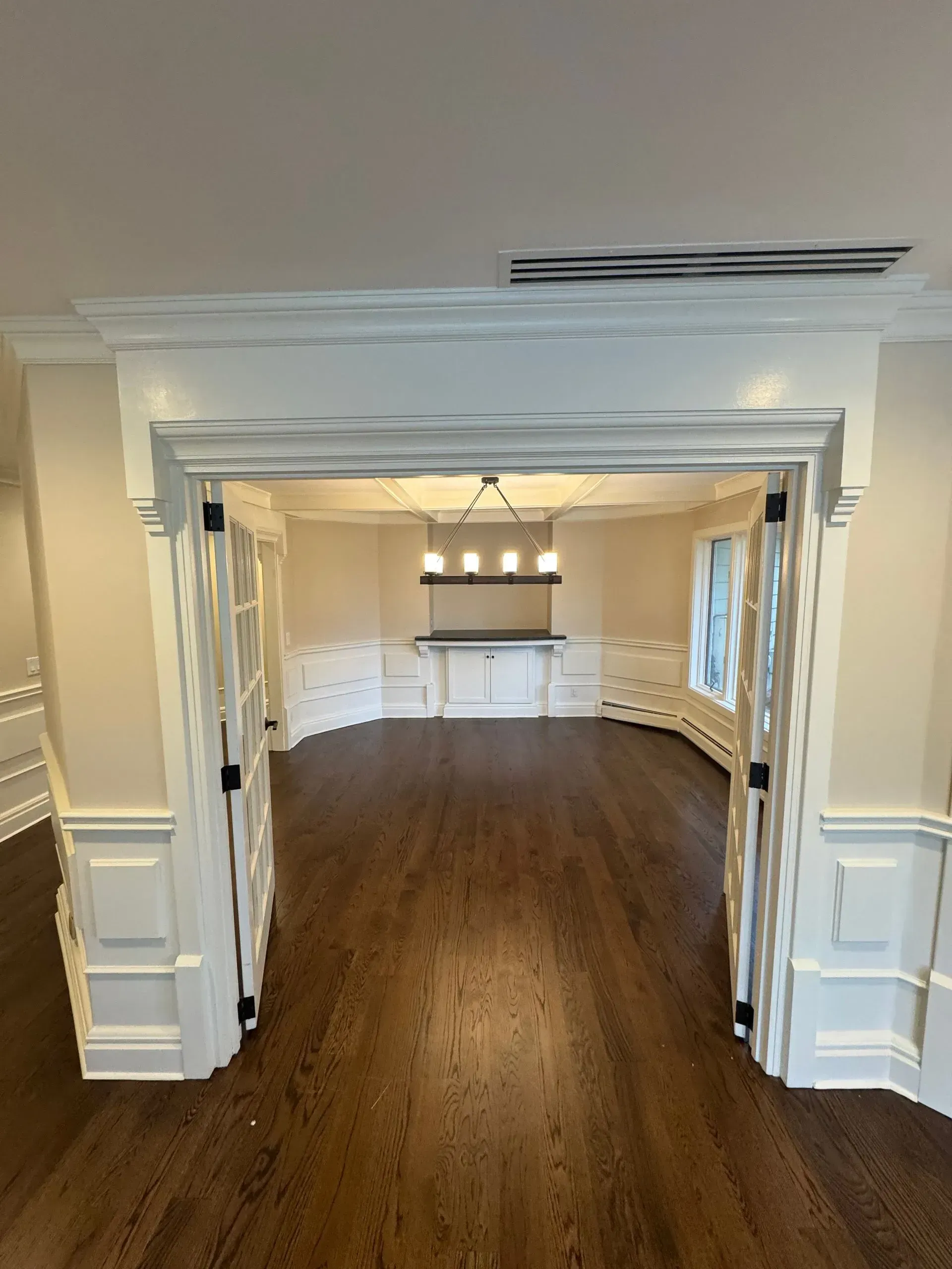 Empty white dining room with dark hardwood floors and a chandelier, viewed through a wide doorway